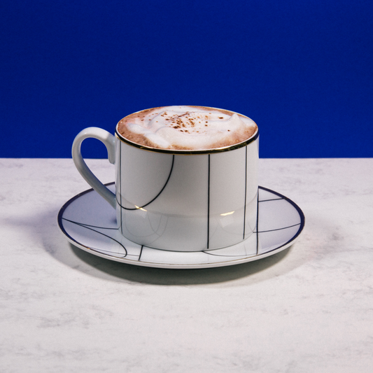 A warm cacao chai latte in a coffee cup with cinnamon and spices on the side
