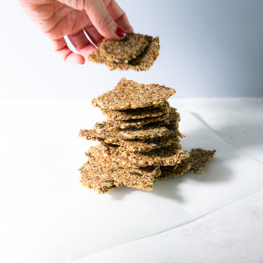 Homemade seed crackers with oats and mixed seeds on baking paper, served with hummus