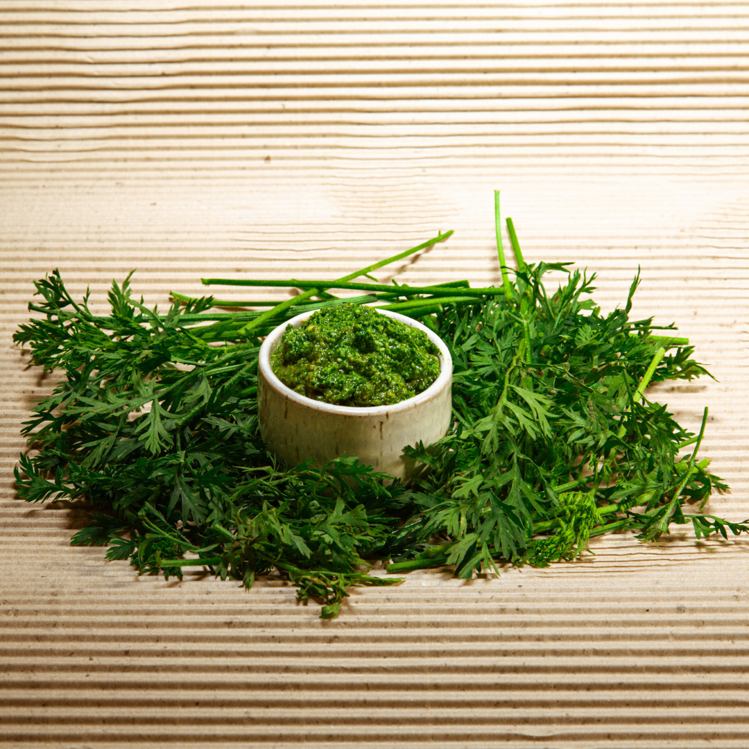 A jar of homemade green pesto made with fresh basil and rocket, surrounded by pine nuts and parmesan