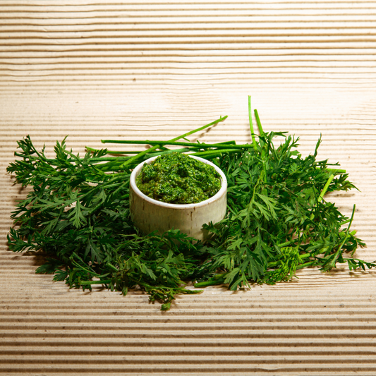 A jar of homemade green pesto made with fresh basil and rocket, surrounded by pine nuts and parmesan