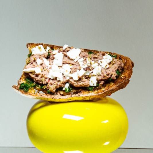 Toasted sourdough bread topped with red bean spread, green pesto, crumbled feta and pine nuts